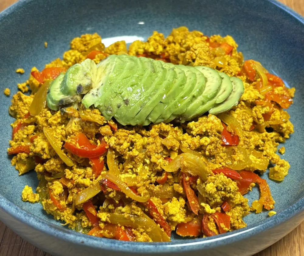 Tofu scramble with red pepper, onion and sliced avocado in a blue bowl